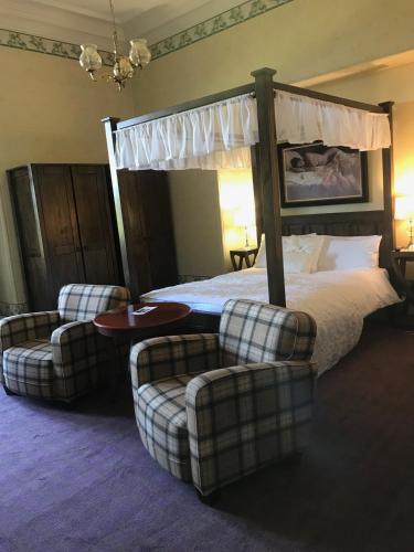 a bedroom with a canopy bed and two chairs at Mansfield House Hotel in Hawick