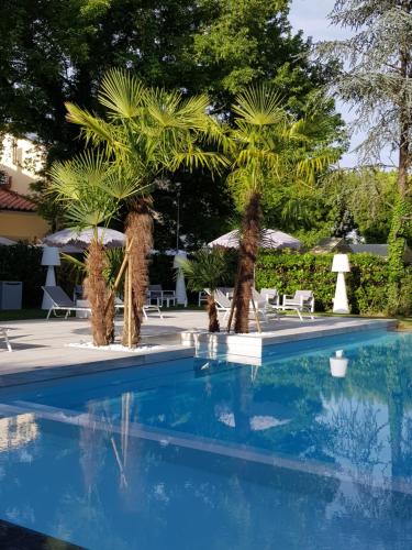 a blue swimming pool with palm trees and chairs at Hotel Hambros - Il Parco in Villa Banchieri in Lucca