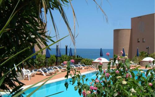 a swimming pool with chairs and umbrellas and the ocean at Addaura Village e Congressi in Mondello