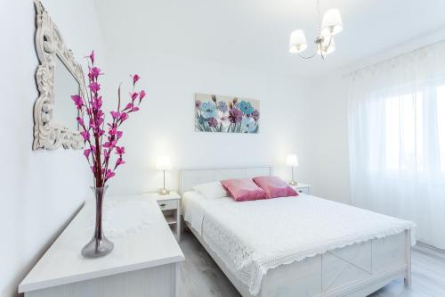 a white bedroom with a bed and a vase with flowers at Guest House Simoni in Prigradica