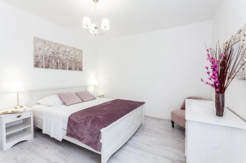 a white bedroom with a bed and a vase of flowers at Guest House Simoni in Prigradica