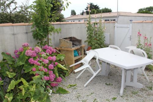 une table et des chaises blanches dans un jardin fleuri dans l'établissement Maison Ile de Ré - Bois Plage en Ré, au Bois-Plage-en-Ré