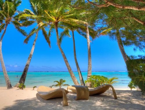 two chairs on the beach under palm trees at Little Polynesian Resort in Rarotonga