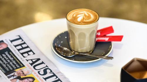 a cup of coffee sitting on a table next to a newspaper at ibis Melbourne - Glen Waverley in Glen Waverley