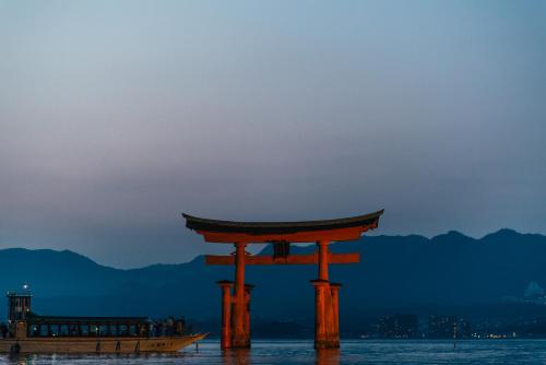 an orange torii gate in the water with a boat at The Evergreen Hostel 長期ステイ歓迎 エバーグリーンホステル in Hiroshima