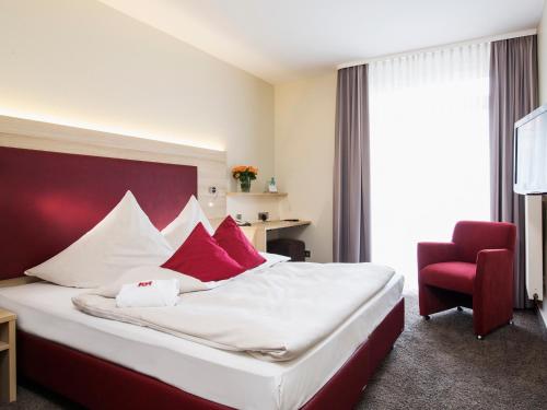 a hotel room with a bed and a red chair at Concorde Hotel am Leineschloss in Hannover