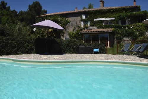 une maison avec un parasol à côté d'une piscine dans l'établissement Ombre Bleue Du Figuier, Ailhon, à Ailhon