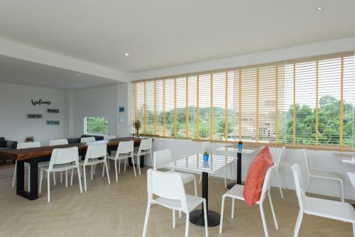 a dining room with white chairs and tables and windows at Costa Village Bangsaray in Bang Sare