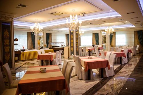 a restaurant with tables and chairs and chandeliers at Jumbaktas Astana Hotel in Astana