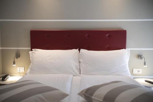 uma cama com cabeceira vermelha e almofadas brancas em Hotel Imperial ***S em Garda