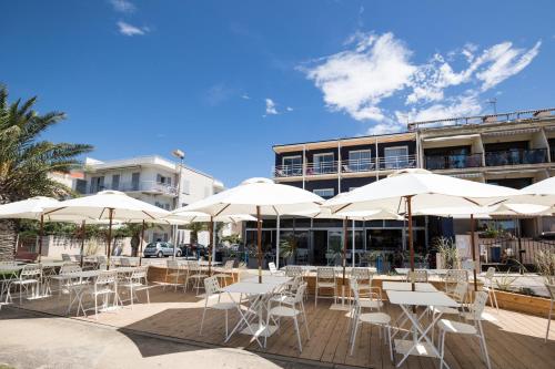 une terrasse avec des tables blanches, des chaises et des parasols dans l'établissement Hôtel Café Miramar, au Grau-du-Roi