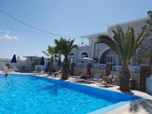 a large swimming pool with palm trees and people in chairs at Alkyon Hotel in Kamari