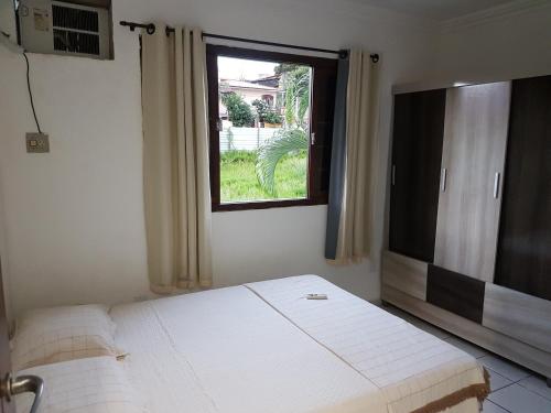 a bedroom with a white bed and a window at Casa em Ponta Negra in Natal
