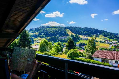 a person reading a book in a balcony with a view of a mountain at Gästehaus Riedl in Warmensteinach