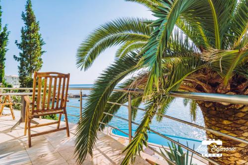 a chair and a palm tree on a balcony overlooking the water at Resort Stikovic in Dobra Voda