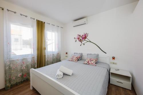 a white bedroom with a large bed with a flower vase on it at apartman Amigo in Kaštela