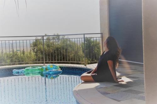 a woman sitting on a ledge next to a swimming pool at Vila Manor in Midrakh ‘Oz