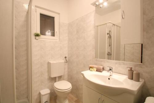 a white bathroom with a toilet and a sink at Apartments Supra Mare in Rabac