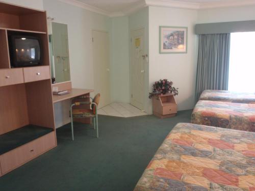 a hotel room with two beds and a desk and a television at Runaway Bay Motor Inn in Gold Coast