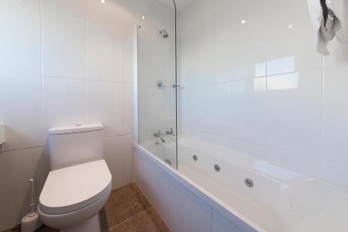 a white bathroom with a toilet and a bath tub at Lakeland Resort Taupo in Taupo