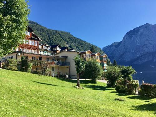 a hotel on a hill with a green field and mountains at Hotel am See - Seeresidenz in Altaussee