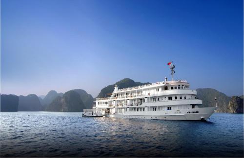 ein großes weißes Boot auf dem Wasser mit Bergen im Hintergrund in der Unterkunft The Au Co Cruise - Managed by Bhaya Cruise in Hạ Long