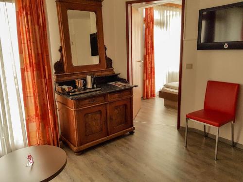 a room with a dresser with a mirror and a red chair at Hotel Bischof in Dornbirn