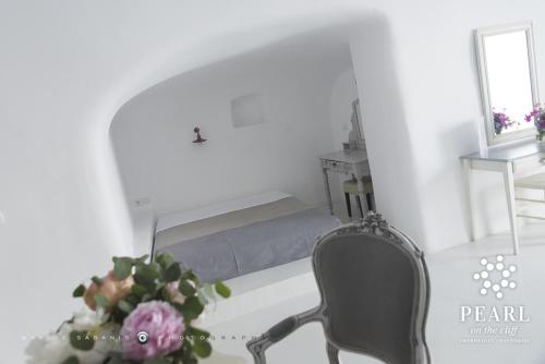 a bedroom with a bed and a chair and a vase of flowers at Pearl on the Cliff Hotel & Suites by Pearl Hotel Collection in Imerovigli