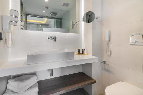 a white bathroom with a sink and a mirror at Hotel Palmyra in Argasi