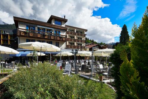 a hotel with tables and umbrellas in front of it at Hotel Spinne Grindelwald in Grindelwald
