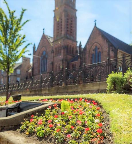 a church with a clock tower and flowers in front of it at Kelpies Serviced Apartments in Falkirk
