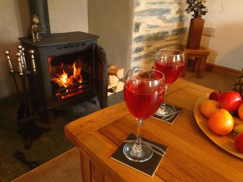 two glasses of red wine on a table with a fireplace at Dolmurgoch Snowdonia Cottage in Dolwyddelan