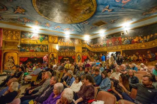 a crowd of people sitting in a room with paintings on the ceilings at Amargosa Opera House & Hotel in Death Valley Junction