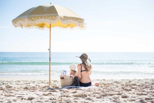 una mujer sentada en la playa bajo una sombrilla en Tingirana Noosa, en Noosa Heads