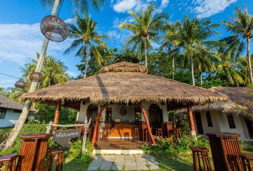 a house with a straw roof and chairs and palm trees at Elixir Koh Yao Yai - SHA Plus in Ko Yao Yai