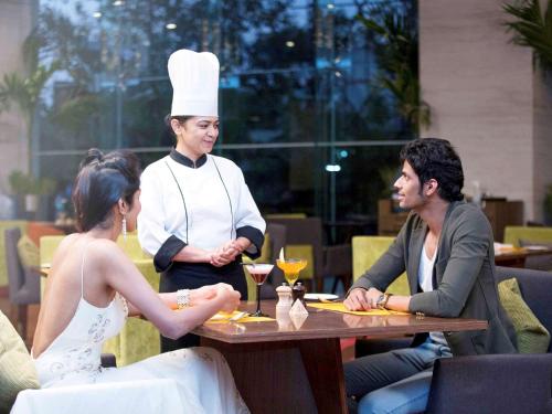 a woman sitting at a table in a restaurant with a chef at Novotel Ahmedabad in Ahmedabad