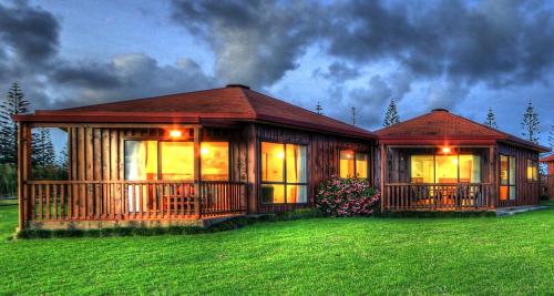 a log cabin with a large deck in the grass at Ocean Breeze Cottages in Burnt Pine