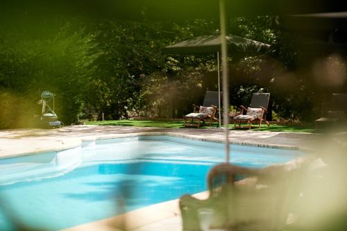 - une piscine avec 2 chaises et un parasol dans l'établissement Castel Bois Marie, Maison d'hôtes, à Montauban