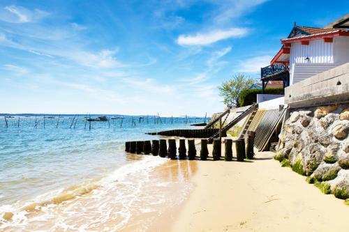 une plage avec un bâtiment et l'eau dans l'établissement Camping Routes du Monde ATC La Hume-Arcachon, à Gujan-Mestras