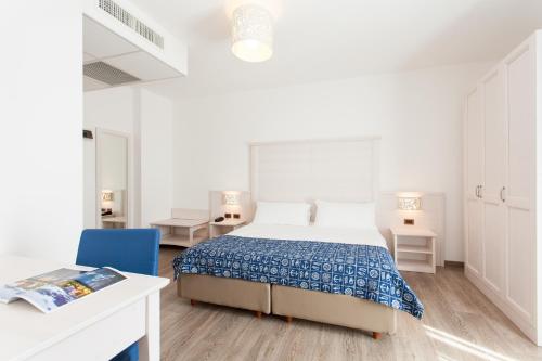 a white bedroom with a bed and a blue chair at Regent's Hotel in Lido di Jesolo