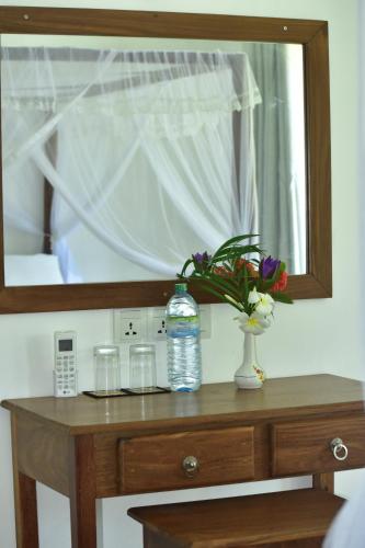 a bottle of water and a vase of flowers on a table at Green Almond Hotel in Unawatuna