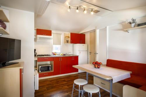 a kitchen with red cabinets and a table with two stools at Valamar Camping Padova in Rab