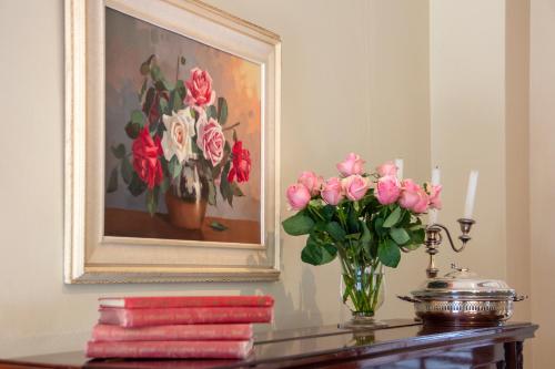 a table with a vase of pink flowers and a painting at De Hoek Manor in Stellenbosch