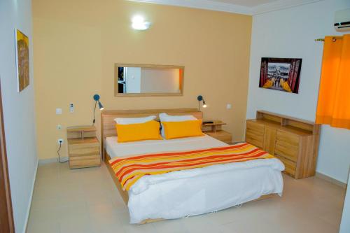 una camera da letto con letto, cuscini arancioni e specchio di Hotel Le Marly a Abidjan