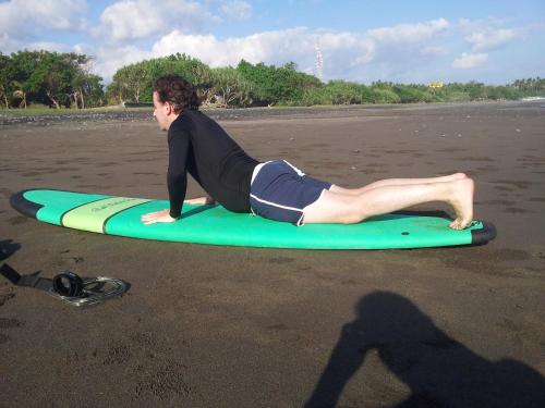 a man laying on a surfboard on the beach at THE NYAMO surf & stay in Pulukan