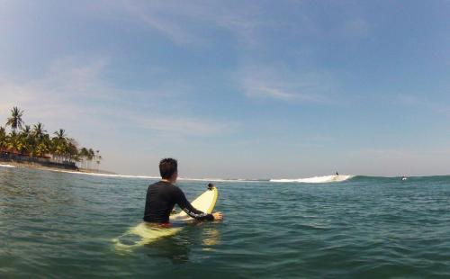 a man sitting on a surfboard in the ocean at THE NYAMO surf & stay in Pulukan