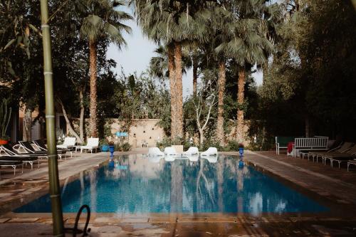 a swimming pool with white chairs and palm trees at Le Bled Ferme in Marrakesh