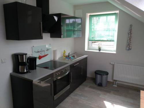 eine Küche mit schwarzen Schränken, einem Waschbecken und einem Fenster in der Unterkunft Pension Holmer Moorhof in Hartenholm