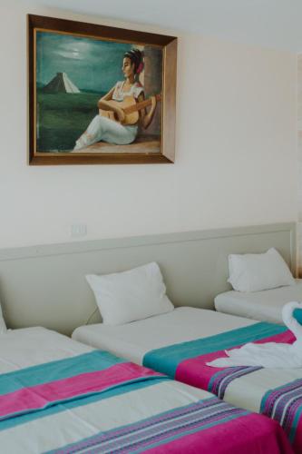 two beds with a painting of a woman playing a guitar at Hotel Ambassador Mérida in Mérida