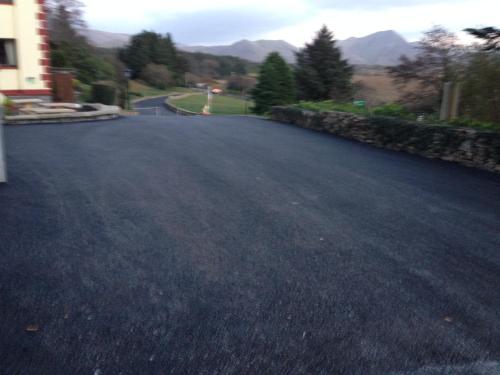 an empty road with a house and mountains in the background at Kylemore Pass Hotel in Letterfrack